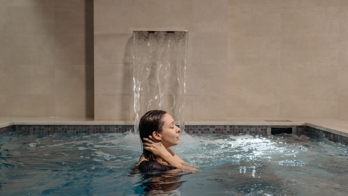 Adult woman relaxing in an indoor swimming pool near a cascading waterfall.